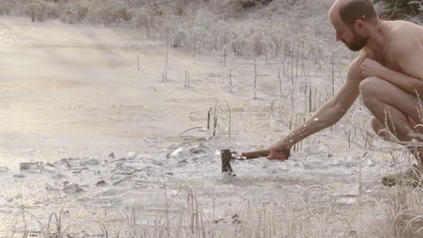 super slow motion - fairly naked ice bather cutting a hole with an axe