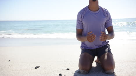 a young biracial man meditates on a sandy beach with copy space