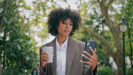 Mujer-Hablando-Por-Teléfono-Videollamada-Caminando-En-El-Parque-De-La-Ciudad-Sostenga-El-Primer-Plano-De-Una-Taza-De-Café-De-Papel.