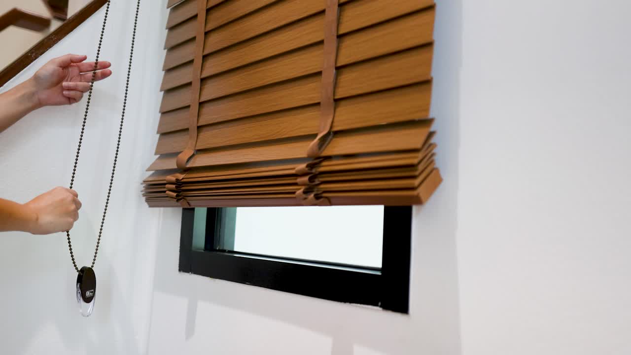 Dichtbijopname van handen die aan een koord trekken om houten jaloezieën op te trekken in een licht interieur.