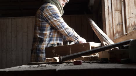 man uses tools to work on parts in workshop with natural light from window