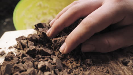 slow motion of female hands preparing chocolate cookies pushing the cut up chocolate into the bowl.