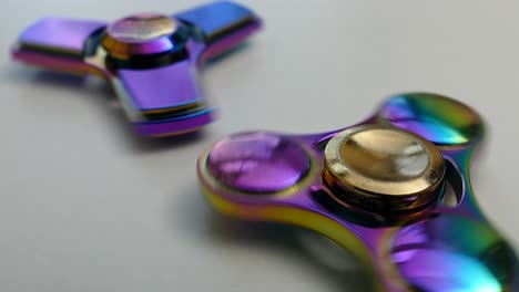 Two-iridescent-fidget-spinners-spinning-on-a-white-surface,-roller-toy-for-kids,-object-for-anxiety