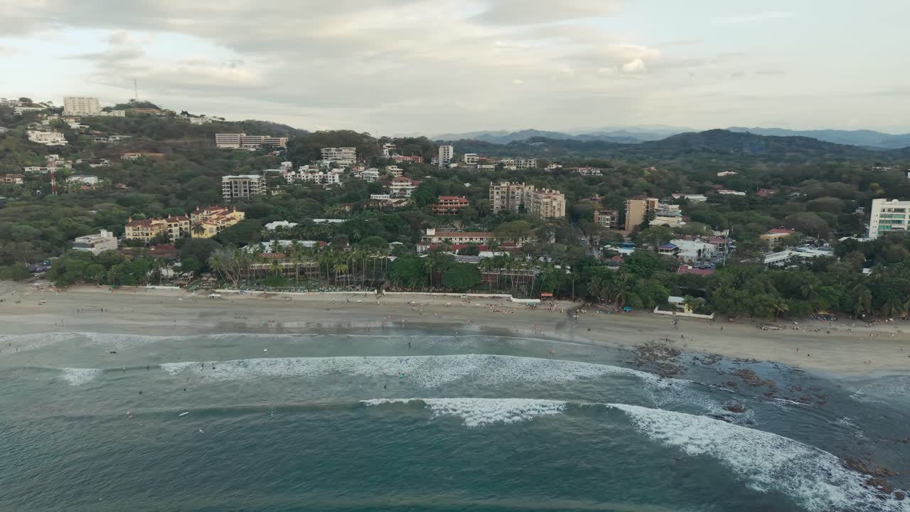 Panoramica aerea verso destra che cattura la costa di Tamarindo con onde, spiaggia e paesaggio tropicale.