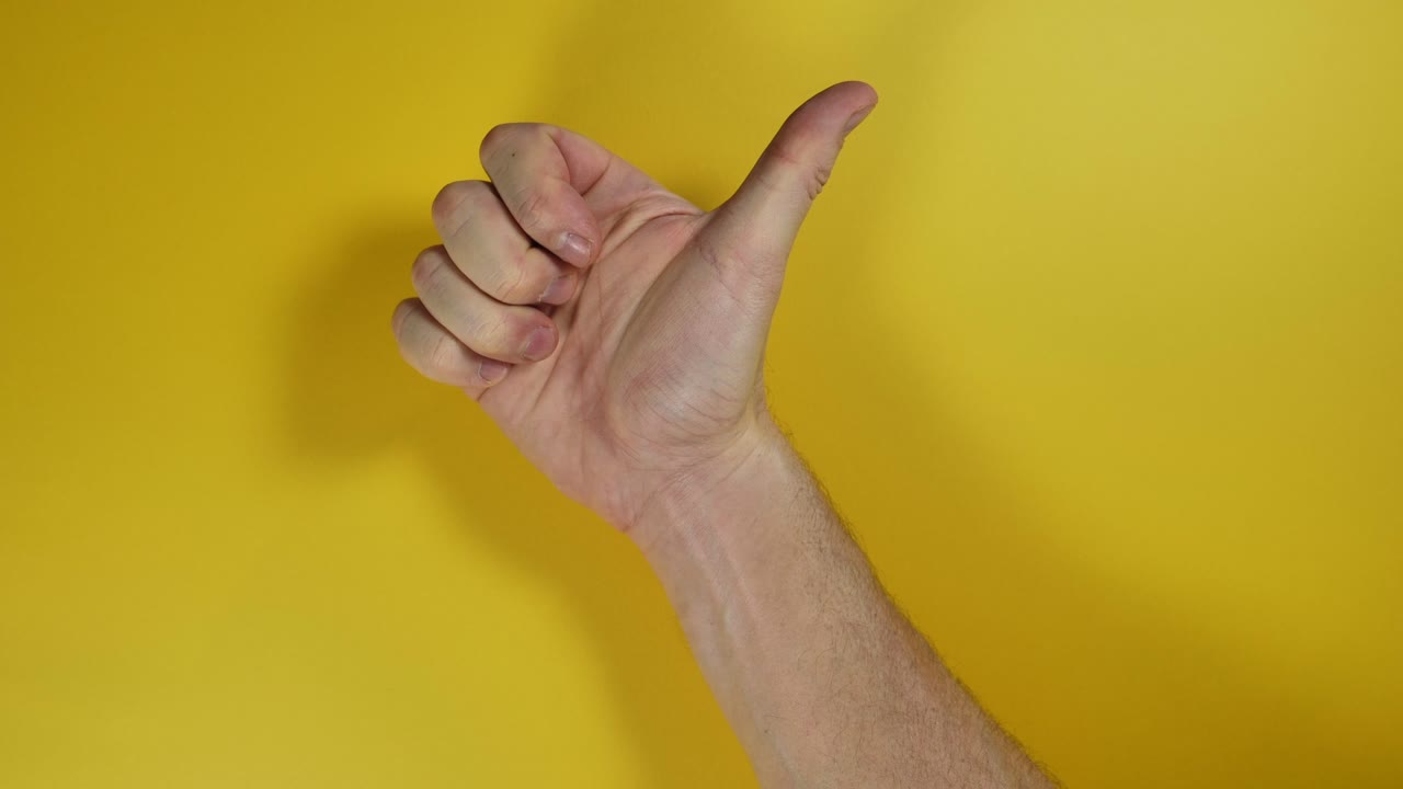 mano masculina haciendo un pulgar positivo hacia arriba sobre fondo de pantalla amarilla