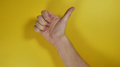 mano masculina haciendo un pulgar positivo hacia arriba sobre fondo de pantalla amarilla