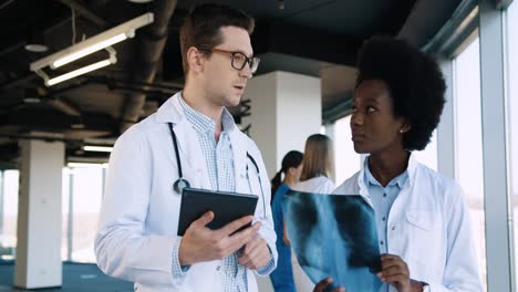 close-up view of caucasian male doctor typing on tablet and discussing xray scan with african american female doctor in hospital