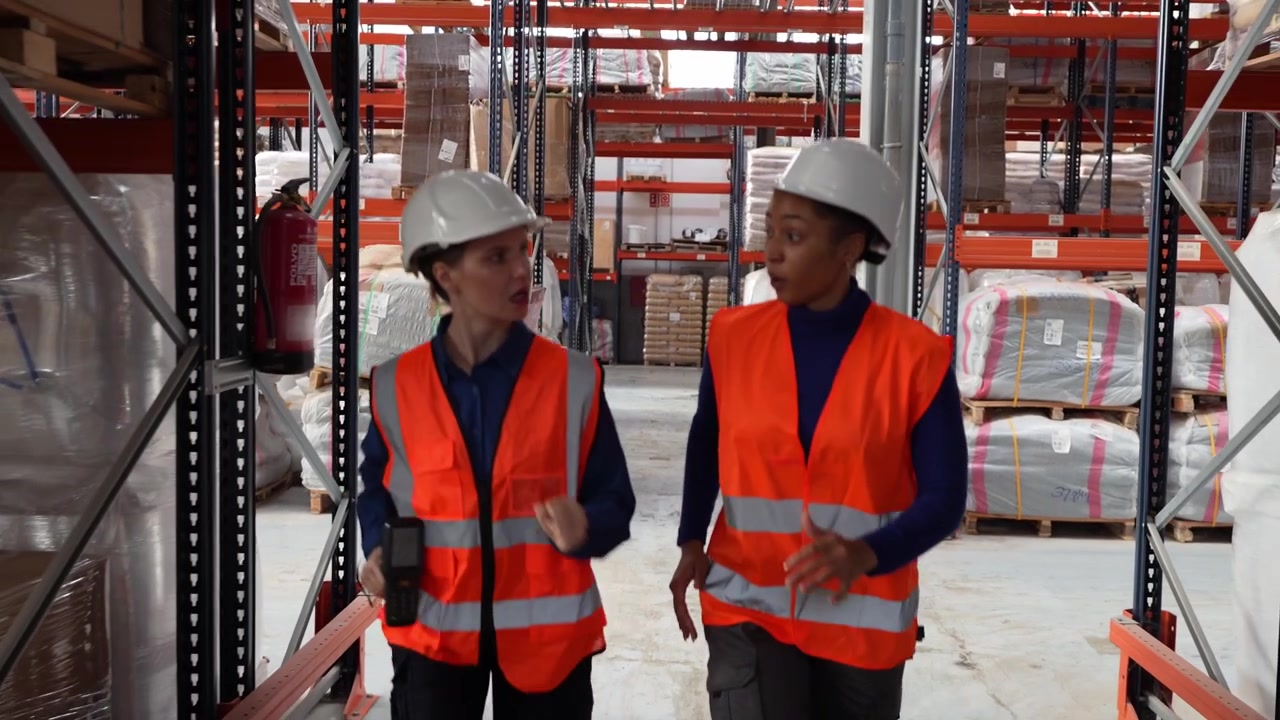 Two Female Warehouse Workers Running Through A Distribution Center