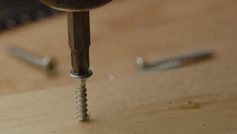 macro view of electric screwdriver drilling screw in wooden board on a construction site in slow motion