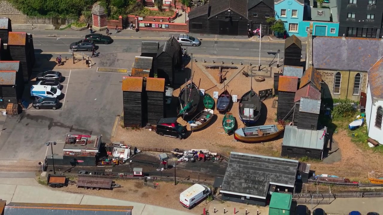 Ikoniske høje sorte træfiskenetshuse, traditionelle fiskerbåde og historisk maritimt kulturarvsområde ved Stade-stranden i Old Town Hastings, East Sussex, Storbritannien, set med drone i kredsløb