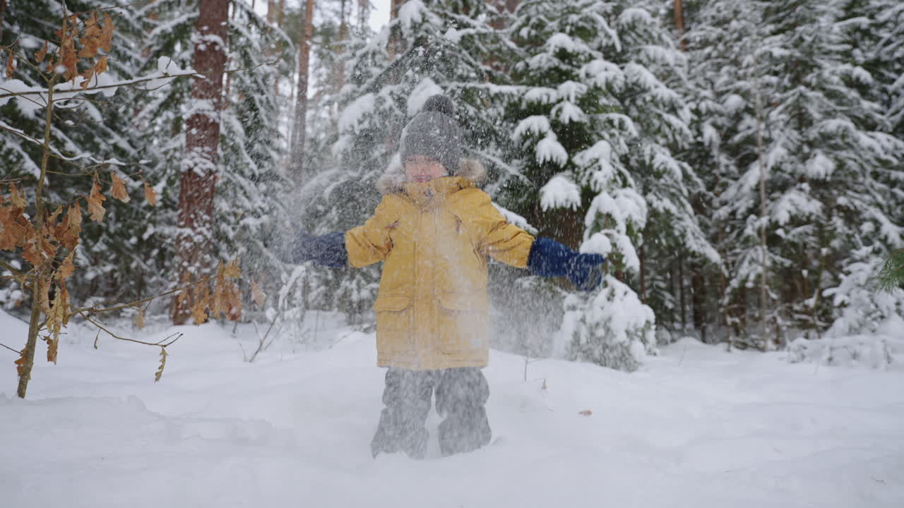 el niño feliz se está divirtiendo en el bosque de invierno arrojando nieve y sonriendo vacaciones de navidad