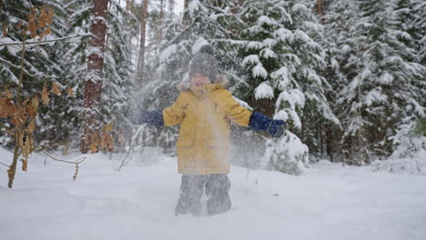 happy little boy is having fun in winter forest throwing snow and smiling christmas vacation