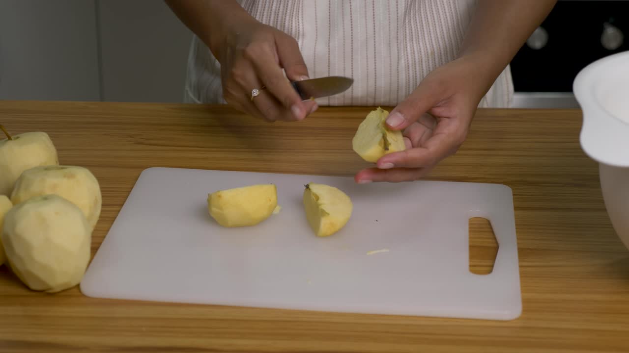 Woman chef remove apple core with knife on white board, light brown table top - Domestic kitchen