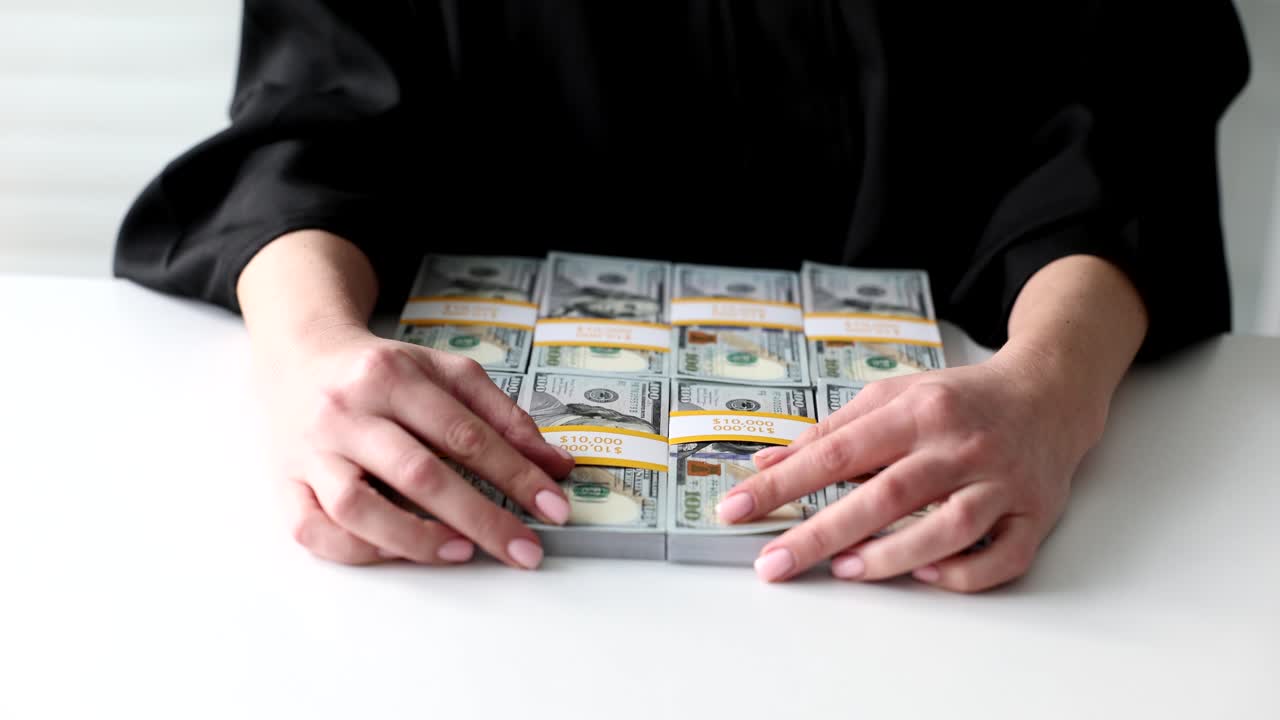 Person's hands on large stacks of hundred-dollar bills