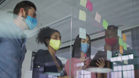 Diversos-Colegas-Que-Usan-Máscaras-Faciales-Usando-Notas-En-Una-Pared-De-Vidrio-Teniendo-Una-Discusión