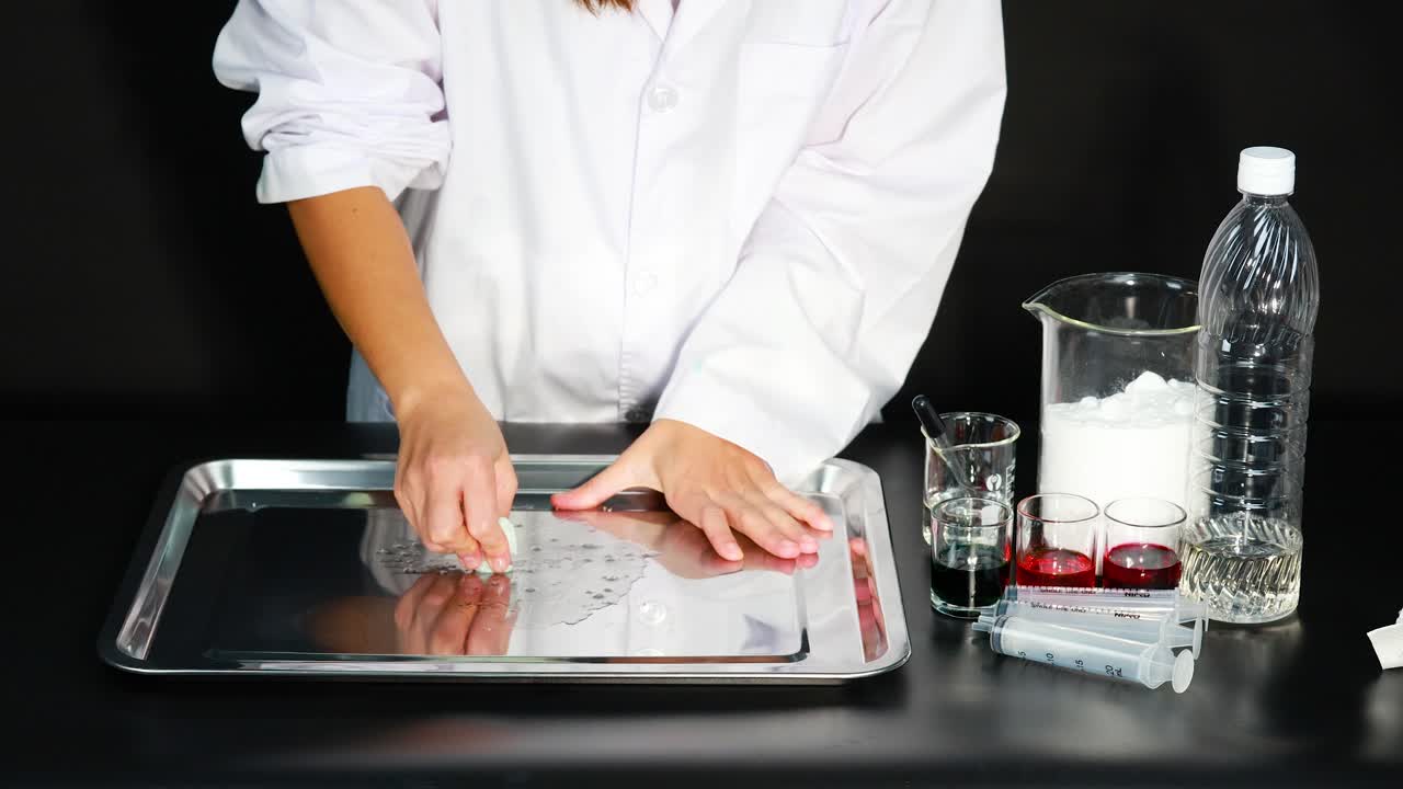 una persona con una bata de laboratorio demuestra técnicas de limpieza en una bandeja usando varios líquidos y materiales