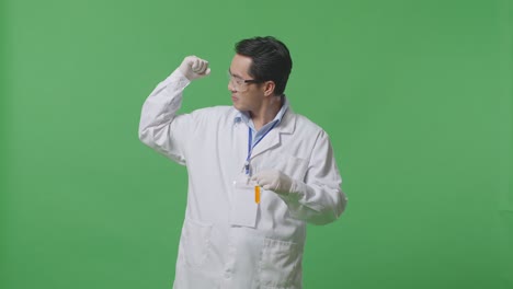 asian man scientist with orange liquid in the test tube smiling and flexing his bicep while standing on the green screen background in the laboratory