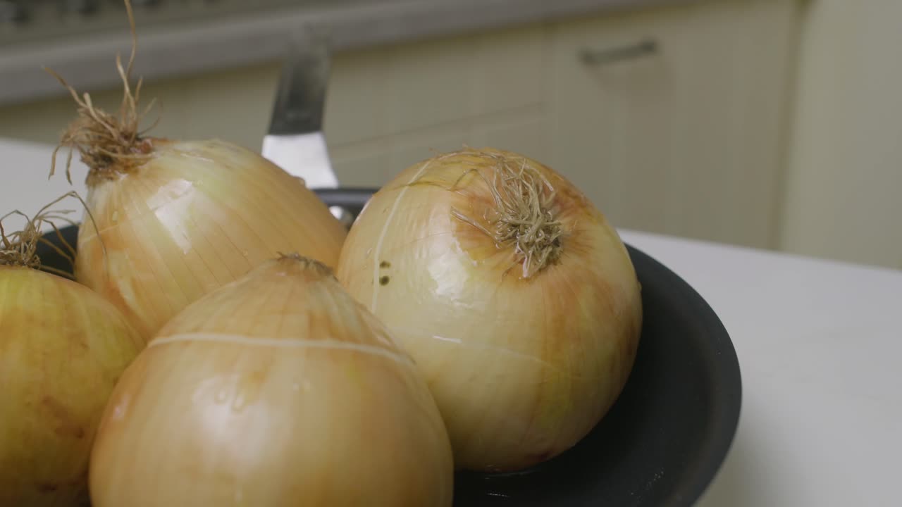 Four yellow onions inside frying pan on kitchen table prepared for baking