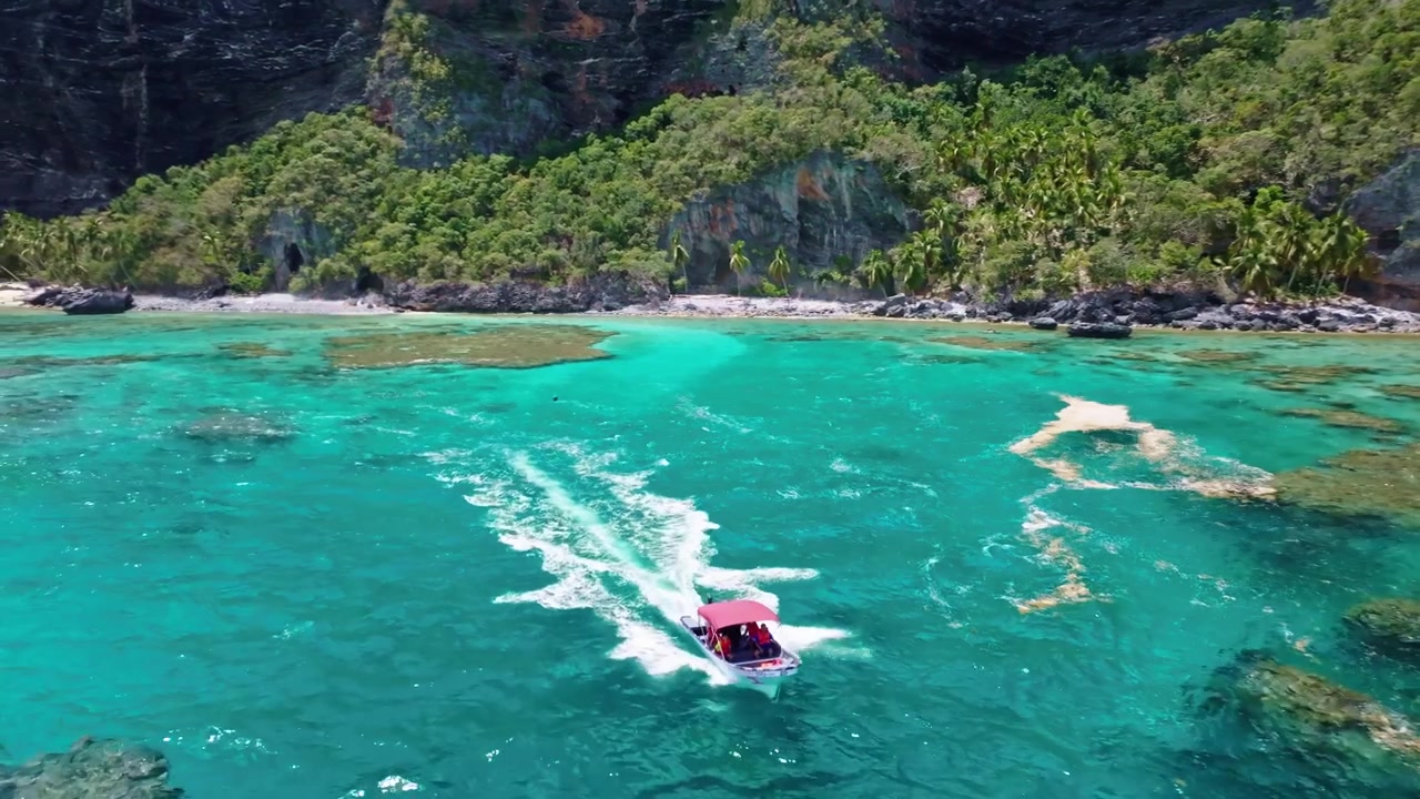 Barca turistica che naviga nelle acque turchesi del mare della spiaggia di Playa Fronton, Samana nella Repubblica Dominicana. Ripresa aerea all'indietro