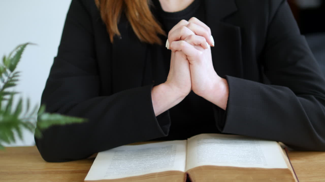 테이블 위 에 있는 개방 된 성서 책 에 손 을  ⁇ 고 손가락 을  ⁇ 어 기도 하는 여자