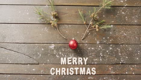 video of christmas greetings text and bauble decoration on wooden background