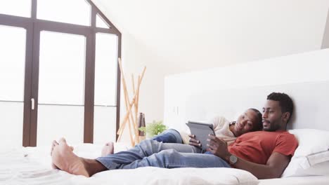 una feliz pareja afroamericana acostada en la cama usando una tableta, en cámara lenta.
