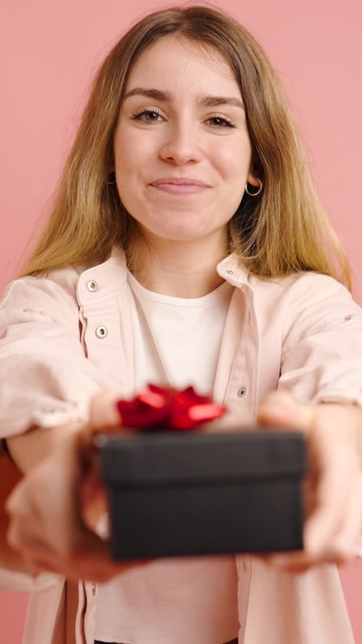 Young woman offering a gift on pink background