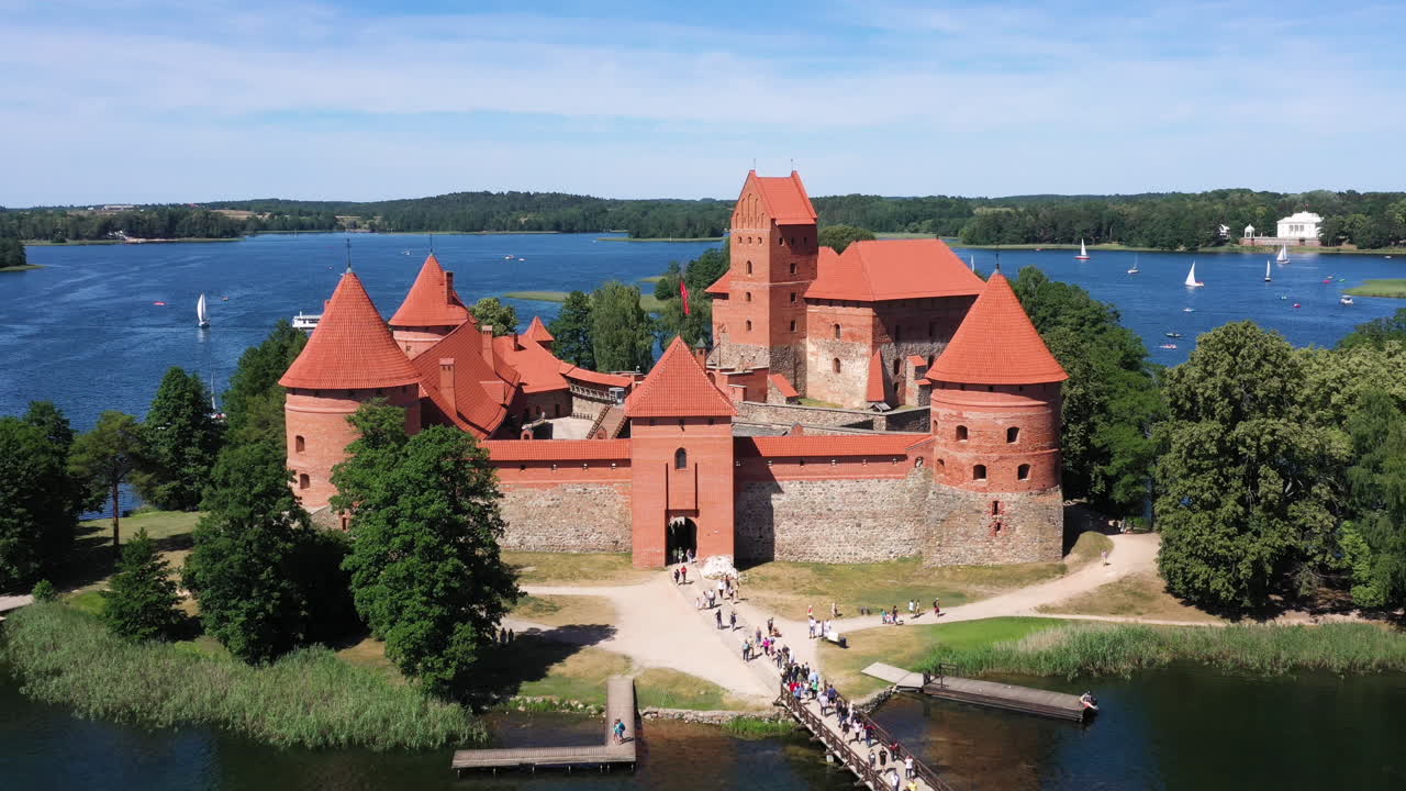 antena: revele la toma del castillo de la isla de trakai junto con un puente de madera y árboles con un cielo azul nublado en el fondo