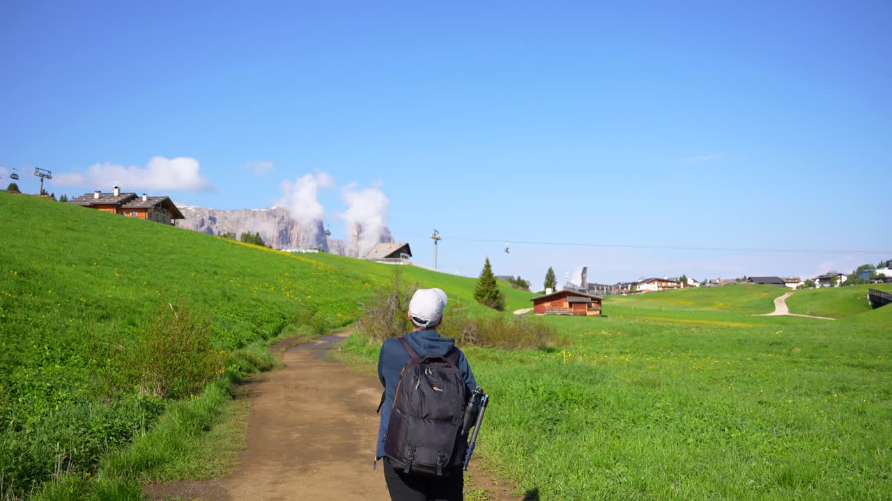 모자를 쓴 남자가 알페 디 시우시 (alpe di siusi, dolomites, italy) 에서 하이킹 경로를 시작하기 위해 배 ⁇ 을 조정합니다.