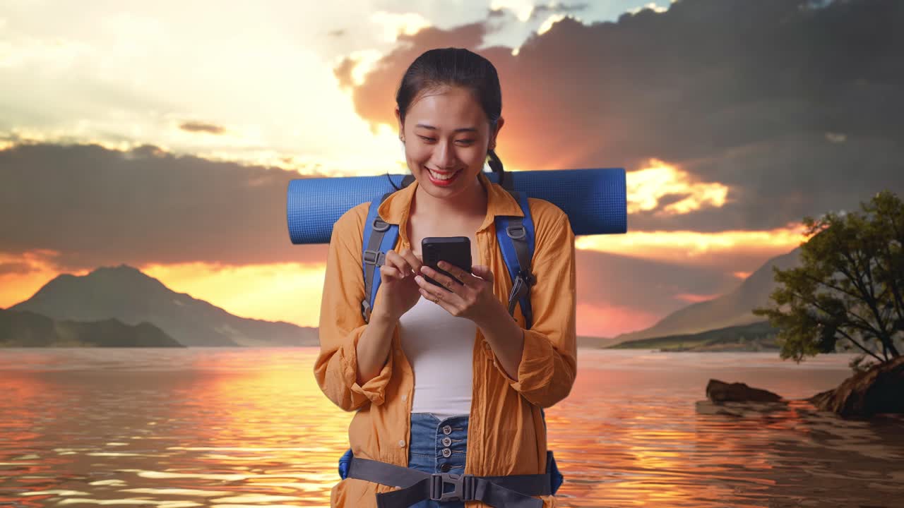 excursionista asiática con mochila de montañismo disfruta usando su teléfono inteligente mientras está de pie en un lago durante la puesta de sol