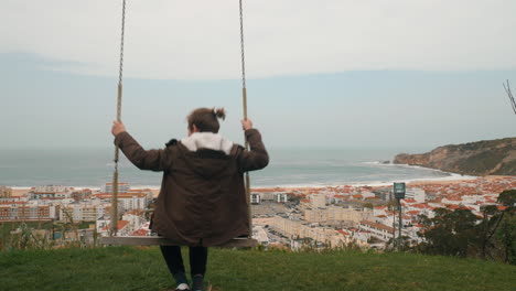 Child-swinging-and-looking-at-ocean-Nazare-scene-Portugal