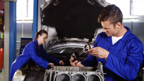 mecánico masculino comprobando las piezas de un coche mientras que la mecánica femenina hace servicio a un coche