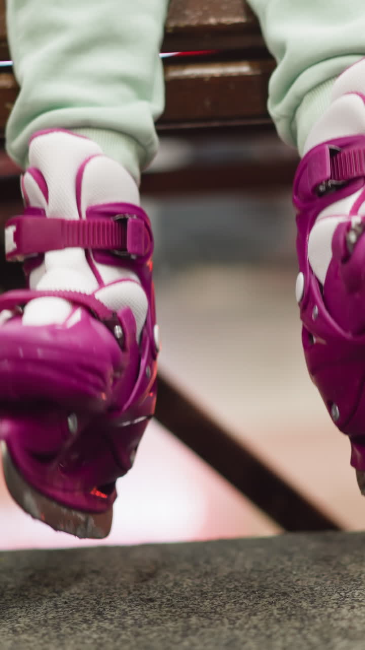 Close-up of a child's feet in pink and white ice skates hanging from a wooden bench, as moving her leg