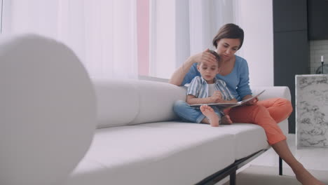 Portrait-of-little-cute-boy-reading-book-with-mother-while-sitting-on-safe