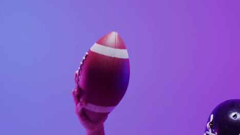 Video-of-caucasian-american-football-player-in-helmet-with-ball-over-neon-purple-background