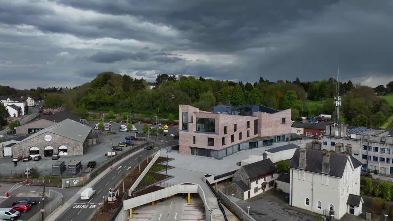 Peace Campus, County Monaghan, Ireland, April 2024. Drone pulls backwards from the Monaghan County Museum into a high angle view of the leafy green trees under dark clouds.
