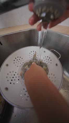 Person washing raw shrimp in a kitchen sink with a colander