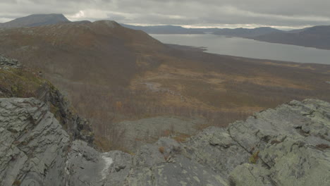 Small-stream-of-water-flows-over-the-edge-with-lake-and-mountains-in-the-backround