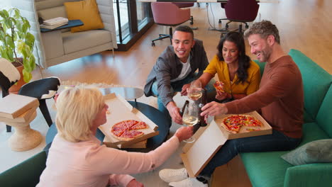 staff at informal meeting in office with takeaway pizza making a toast with drinks