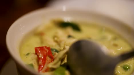 close-up video of thai green curry being stirred, showcasing vibrant ingredients and rich textures in a warm, inviting setting