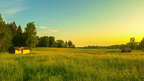 toma estática de cielo amarillo y azul sobre campos de hierba verde con una pequeña cabaña en el tiempo de la tarde en lapso de tiempo