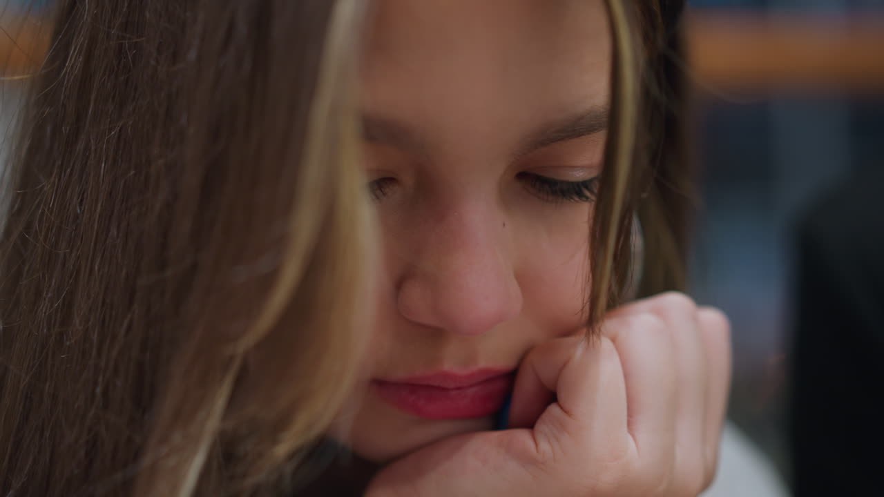 Close up of young lady resting hand under jaw while operating phone with red and blue nail paint focus on modern lifestyle youth culture technology usage with partial view of another person