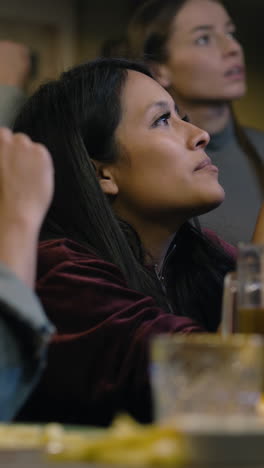 Vertical-shot-of-African-American-fan-celebrating-with-friends-when-football-team-scores-goal-and-wins-the-tournament.-Group-of-multicultural-friends-watch-live-soccer-match-sitting-in-sports-bar-or-pub.