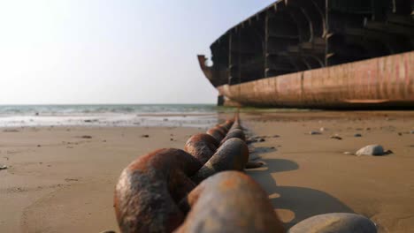 cadena de anclaje oxidada colocada en la playa conectada al barco desmantelado