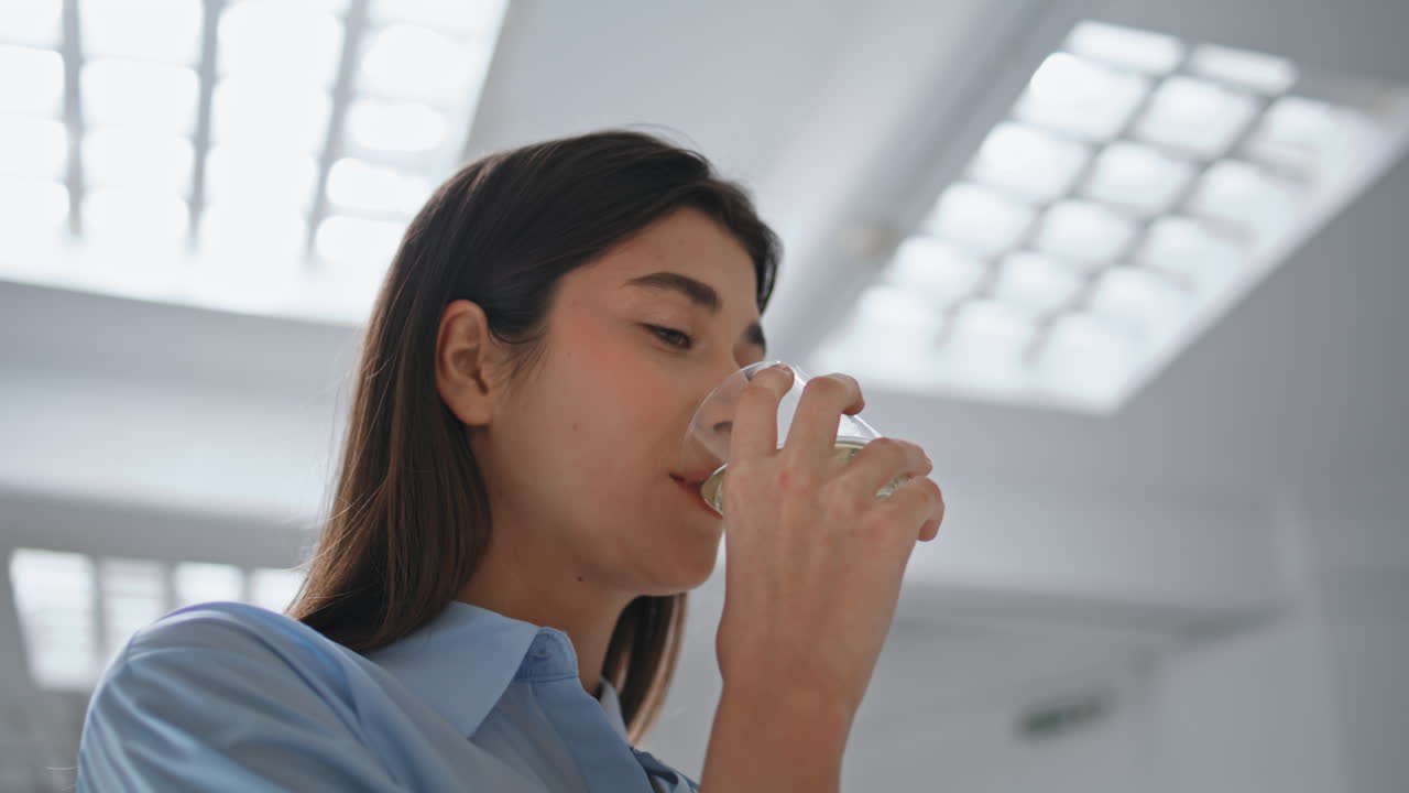 Ragazza sorridente che beve acqua in ufficio, in primo piano. Affarista felice che sorseggia.