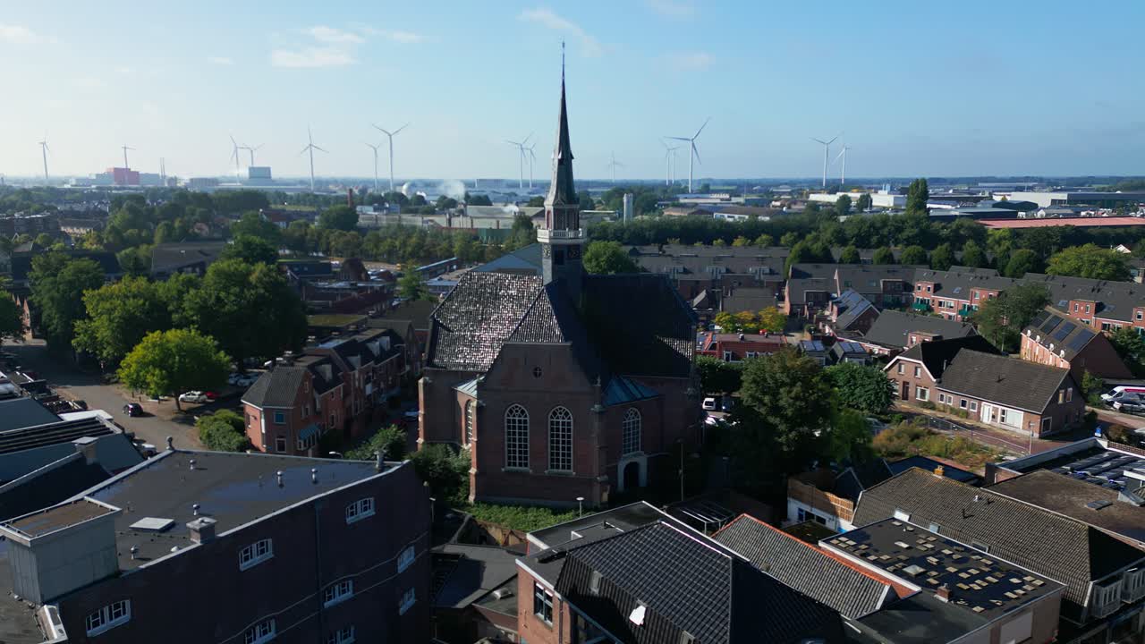 Drone view of Coevorden church with tall spire amid residential rooftops and distant wind turbines. Captured in Coevorden, Drenthe, Netherlands (Coevorden, Drenthe, Nederland)