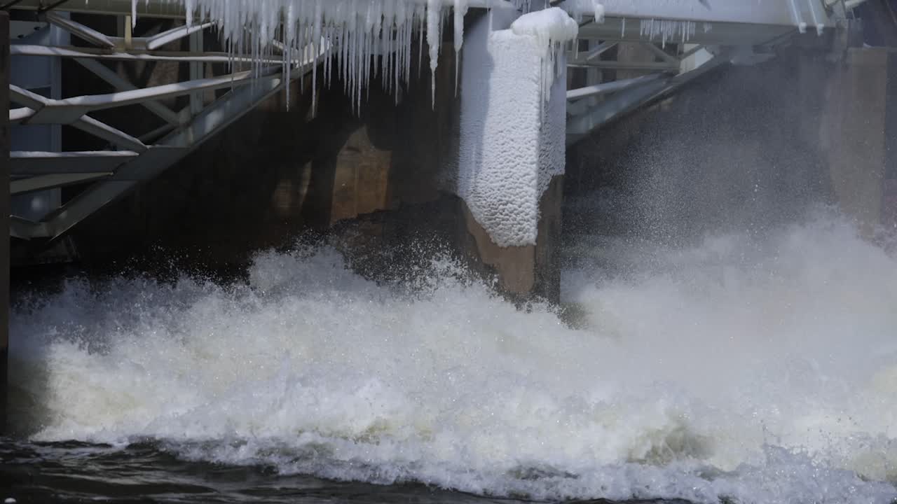 River flowing through dam with some ice on dam close up in slow motion.