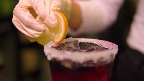 waitress with white protective gloves is putting lemon on the edge of sugared glass filled with fruity cocktail slow motion