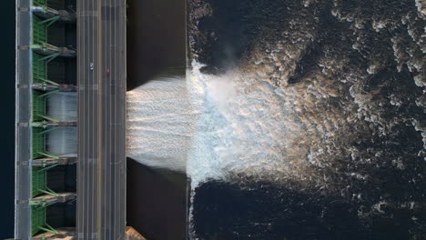 aerial drone view of a powerful water body flowing to a reservoir and a dam below a highway