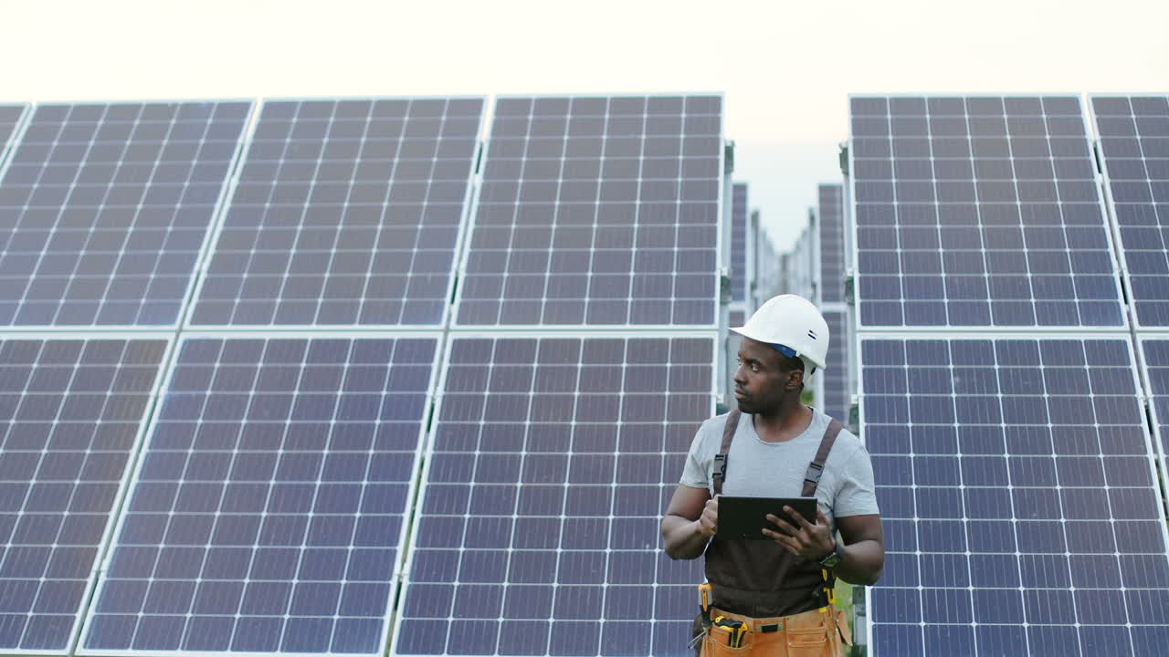 Young african american male engineer standing outside near solar panels and using a tablet